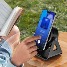 Load image into Gallery viewer, Person using a smartphone with Wireless Induction Speaker with Bluetooth-compatible Speaker while reading a book outdoors.
